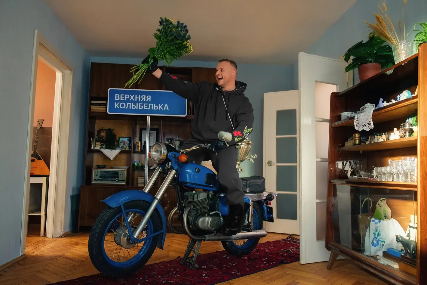 Дима на синем мотоцикле в комнате с сервантом и дорожным знаком